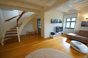 A spacious living area with a wooden staircase, a flat-screen TV, a sofa, and a unique white ottoman. - Holiday home with 3 bedrooms (Ostseebad  Prerow)