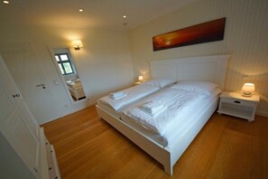 A bedroom with a double bed, bedside tables with lamps, a door with a mirror, and a painting on the wall. - Holiday home with 3 bedrooms (Ostseebad  Prerow)