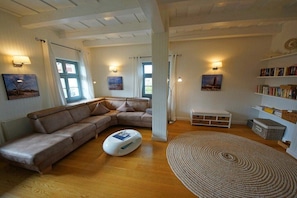 A living room with a sectional sofa, a white ottoman, a round rug, and a bookshelf. - Holiday home with 3 bedrooms (Ostseebad  Prerow)