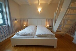 A double bed with white linens in a room with striped wallpaper and a wooden floor. - Holiday home with 3 bedrooms (Ostseebad  Prerow)