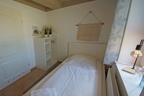 Ein Schlafzimmer mit einem Bett, einem Nachttisch mit Lampe, einem Heizkörper, einem Kleiderschrank und einem Fenster mit Vorhang.