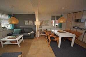 Ein modernes Wohnzimmer mit einer Couch, Couchtisch, Esstisch, Korbstühlen und Pendelleuchten.