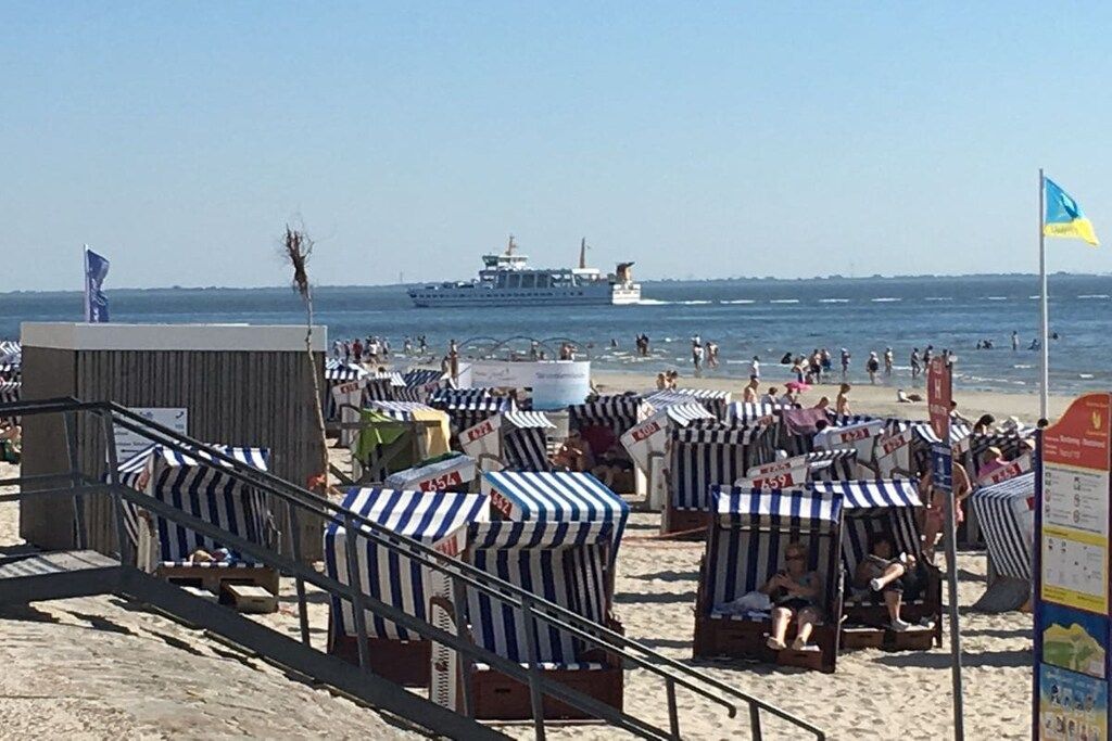 A beach with striped beach chairs and a ship in the background.