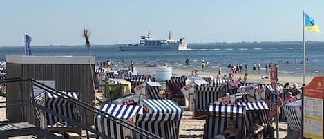 A beach with striped beach chairs and a ship in the background.