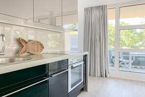 Eine moderne Küche mit Einbauofen, Spüle aus Edelstahl und einem großen Fenster mit Vorhängen.