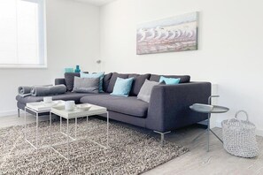 Ein modernes Wohnzimmer mit einem grauen Ecksofa, einem weißen Couchtisch und einem grauen Teppich.