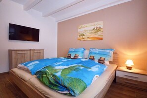 Een slaapkamer met een bed, een aan de muur bevestigde televisie, een nachtkastje met een lamp en een schilderij.