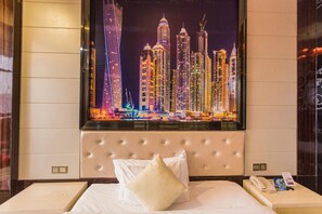 A hotel room with a large cityscape view on the wall, a tufted headboard, a bed with white linens, and a bedside table with a phone and a brochure. - Diy Bai Hotel (Zhanjiang)