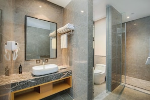 Un baño moderno con lavamanos de mármol, un espejo grande, cabina de ducha de vidrio y un inodoro.