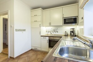 A kitchen with white cabinets, a stainless steel sink, a microwave, and a stove. - Holiday home with 1 bedroom (Wenningstedt)
