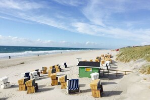 A beach with rows of wicker beach chairs and a small green structure, likely a changing room or storage. - Holiday home with 1 bedroom (Wenningstedt)