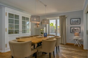 A dining area with a wooden table and chairs, a white cabinet with glass doors, and two hanging wicker lamps. - Holiday home with 1 bedroom (Wenningstedt)