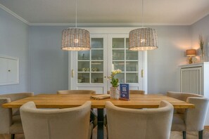 A dining area with a wooden table and chairs, two hanging wicker lamps, and a white cabinet with glass doors in the background. - Holiday home with 1 bedroom (Wenningstedt)