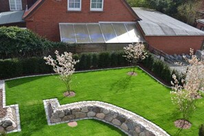 A residential property with a well-maintained lawn, a stone retaining wall, and a brick house with a large window. - Holiday apartment in Juist with swimming pool (Juist)