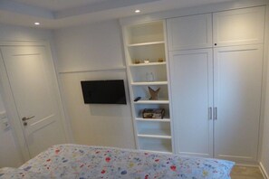 A bedroom with a bed, a television mounted on the wall, and built-in white cabinets. - Holiday apartment in Juist with swimming pool (Juist)