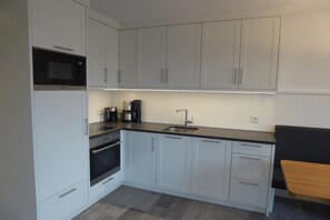 A compact kitchen with white cabinets, a microwave, an oven, a sink, and a coffee maker. - Holiday apartment in Juist with swimming pool (Juist)