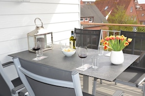 An outdoor dining area with a table set for two, a wine bottle, glasses, and a vase with tulips. - Holiday apartment in Juist with swimming pool (Juist)