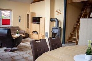 Ein Wohnzimmer mit einer Couch, einem Esstisch mit Stühlen, einem Fernseher, einem Kamin und einer Treppe.
