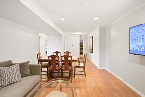 A modern living room with a glass coffee table, a sofa, and a dining area with wooden chairs and a table. - 2BR Suite - Close to Big White, Airport, and Downtown! (Kelowna)