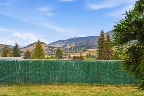 A residential area with a green fence, houses, and mountains in the background. - 2BR Suite - Close to Big White, Airport, and Downtown! (Kelowna)