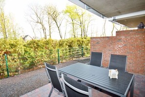 Eine Terrasse im Freien mit Tisch und Stühlen, einer Ziegelwand und einem Metallzaun.