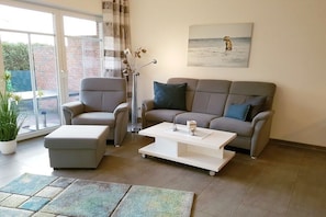 A living room with a sofa, armchair, ottoman, coffee table, and a potted plant. - Holiday apartment with 1 bedroom (Norden-Norddeich)