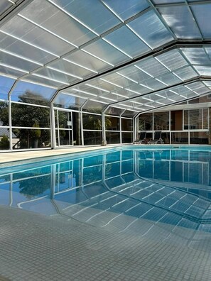 A clear pool with a glass ceiling, surrounded by a tiled deck. - Alojamiento Carilo Princes (Carilo)