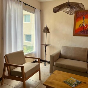 Un soggiorno con un divano, una poltrona, una lampada da terra e un quadro appeso al muro.