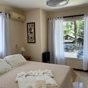 A hotel room with a bed, a wall-mounted air conditioner, a window with curtains, and a view of the outside. - Alojamiento Carilo Princes (Carilo)