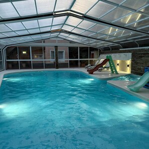 An indoor swimming pool with a glass ceiling, slides, and lounge chairs. - Alojamiento Carilo Princes (Carilo)