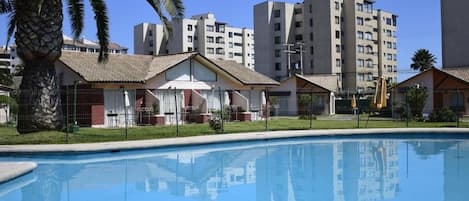 A swimming pool with a clear blue water surface, surrounded by residential buildings and a palm tree.