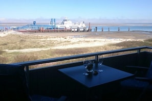 A table with a glass and a bottle, overlooking a beach with a pier and a boat. - Apartment with a view of the islands (Wittdün \/ Amrum)