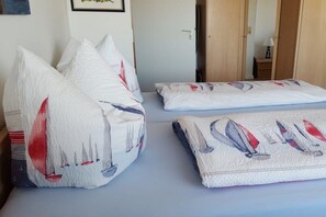 A bed with white pillows and a blanket featuring sailboat designs. - Apartment with a view of the islands (Wittdün \/ Amrum)