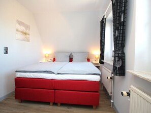 A bedroom with a bed, bedside lamps, a radiator, and a window with curtains. - Holiday Home With 2 Bedrooms (Sylt)