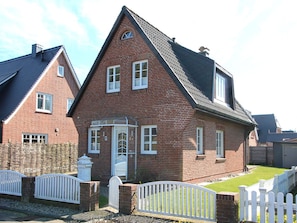 A red brick house with a white door and windows, a small porch, and a white picket fence. - Holiday Home With 2 Bedrooms (Sylt)