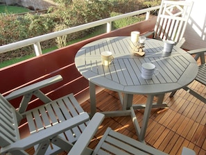Ein runder Tisch mit weißem Tuch, eine Bank und ein Geländer auf einer Holzterrasse.