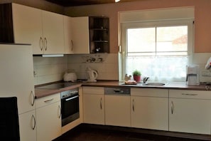 A kitchen with white cabinets, a stove, a sink, and a window with a view. - Holiday home in Hooksiel with swimming pool (Hooksiel)