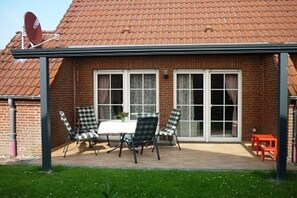 A patio with a table and chairs, a brick building with a tiled roof, and a satellite dish. - Holiday home in Hooksiel with swimming pool (Hooksiel)