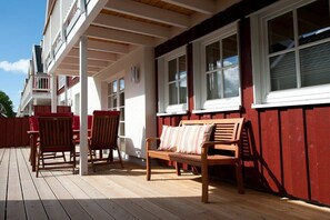A wooden deck with outdoor furniture, including chairs and a bench, adjacent to a building with red siding and white trim. - Holiday apartment in Ahaus with swimming pool (Ahaus)