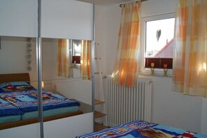 Un dormitori amb un llit, una finestra amb cortines, un radiador i un mirall.