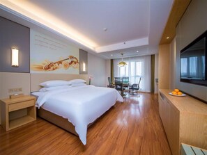 A hotel room with a large bed, a desk, a flat-screen TV, and a dining area with a table and chairs. - Vienna International Hotel (Yichang)