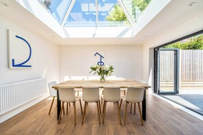 Een moderne eetruimte met een grote tafel, zes stoelen, een bloevas en een dakraam erboven.