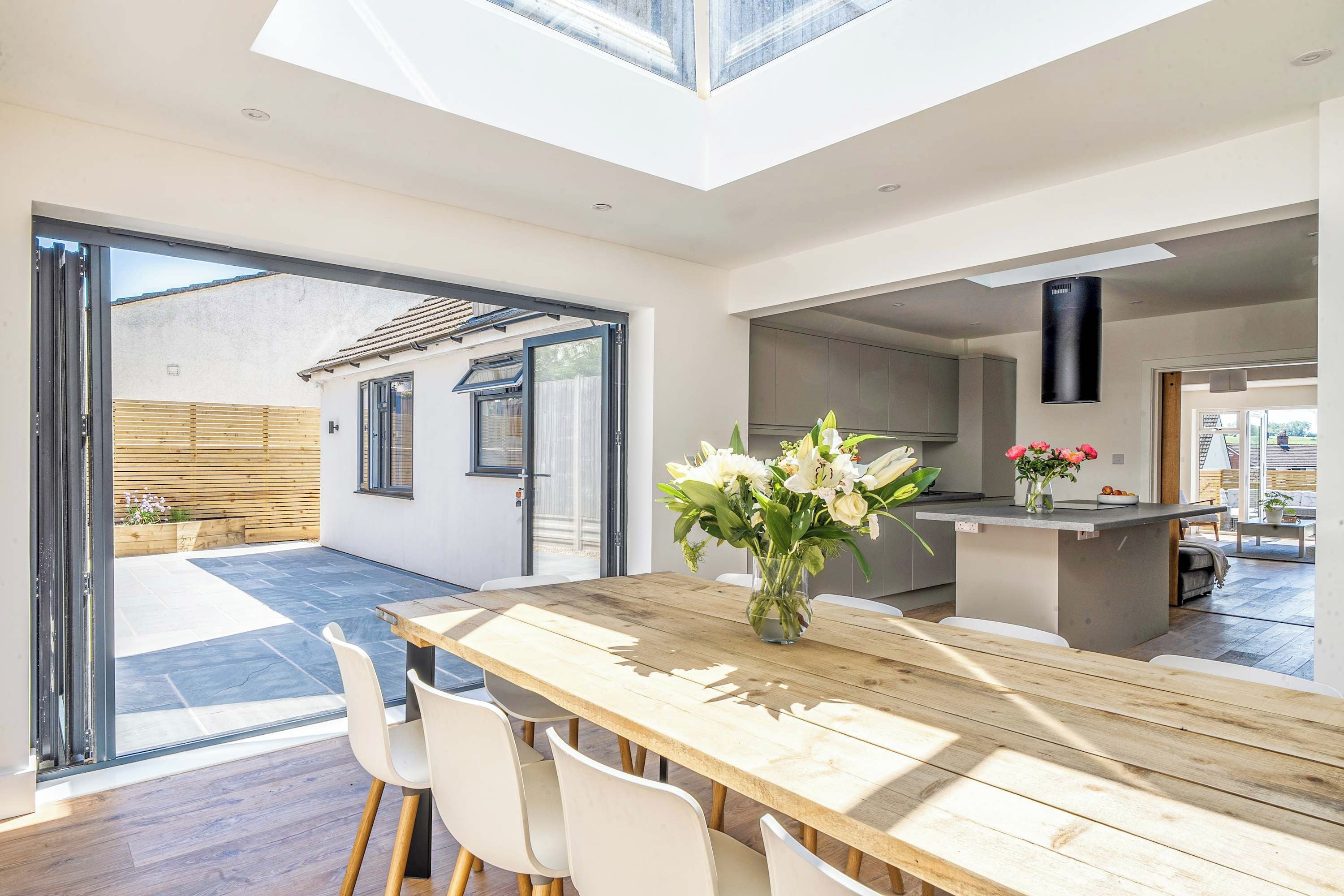 A modern kitchen with a central island, large windows, and a dining area with a wooden table and chairs.