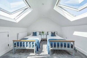 Een slaapkamer met twee bedden, een radiator, een nachtkastje en dakramen.