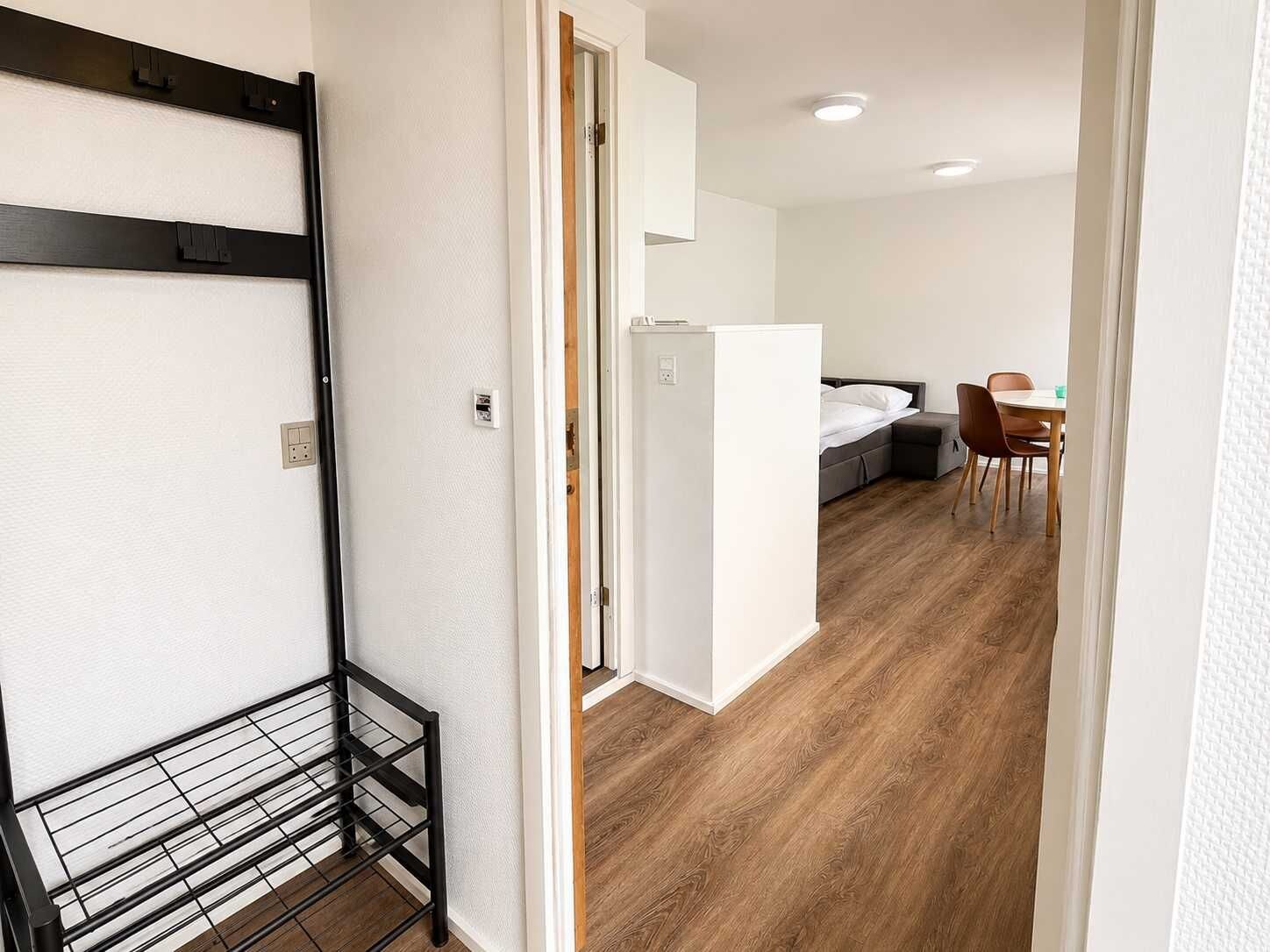 Un pasillo que conduce a un dormitorio con una cama, un escritorio y una silla.