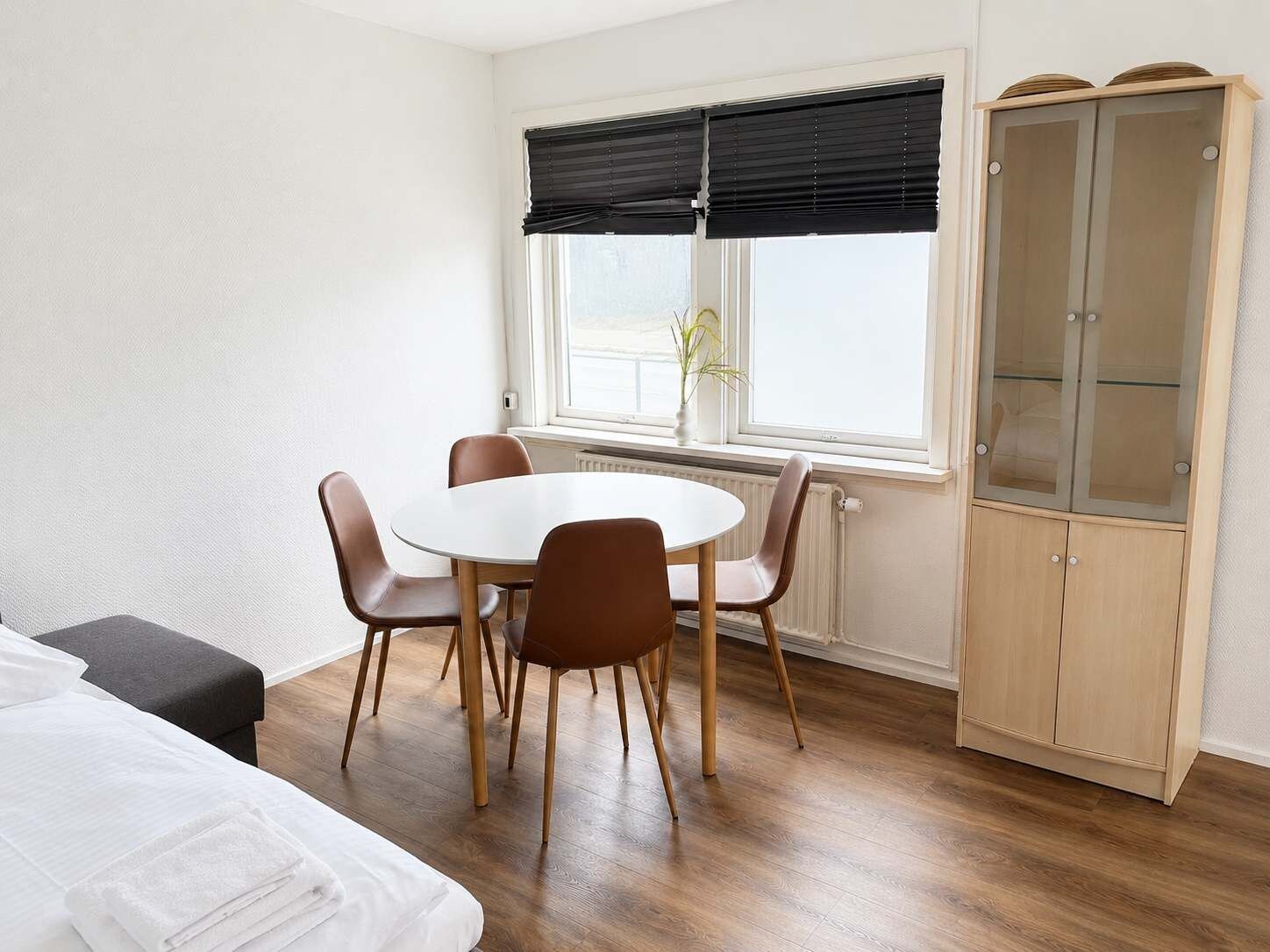 Una habitación con una mesa redonda, cuatro sillas, un armario y una ventana con persianas.