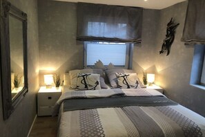 A bedroom with a bed, bedside lamps, a window with blinds, and a wall-mounted artwork. - Holiday apartment with 1 bedroom (Norddeich)