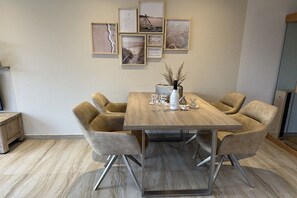 Un coin repas avec une table en bois et quatre chaises, un vase contenant des plantes séchées et des œuvres d’art encadrées accrochées au mur.