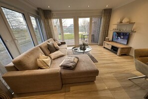 A modern living room with a sofa, coffee table, and television. - Holiday apartment with 1 bedroom (Norddeich)