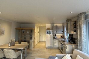 Une cuisine moderne équipée d’un four à micro-ondes, d’une cuisinière et de placards. Un coin repas avec une table et des chaises est également disponible.